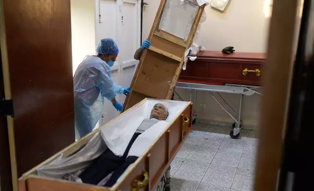 Funeral workers prepare the body of Rosa Elena Gonzalez, 80, who died after her apartment was hit during a U.S. strike to capture President Nicolas Maduro, in Catia La Mar, Venezuela, Sunday, Jan. 4, 2026. (AP Photo/Matias Delacroix)