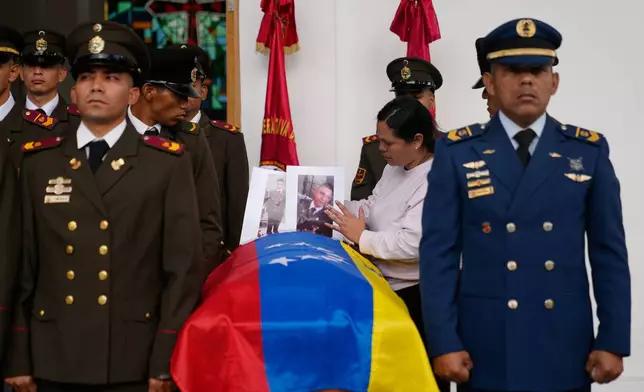 A relative places photographs on the casket of a soldier killed in the U.S. raid to capture Venezuelan President Nicolas Maduro and his wife during a funeral in Caracas, Venezuela, Wednesday, Jan. 7, 2026. (AP Photo/Ariana Cubillos)