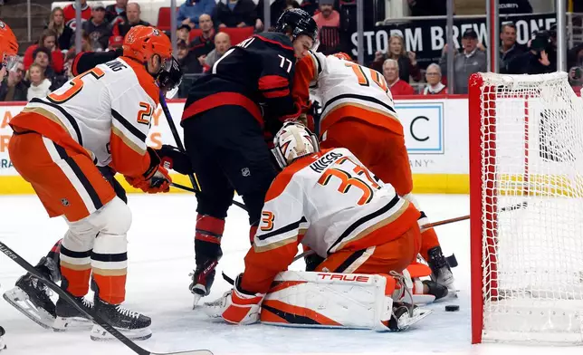 Carolina Hurricanes' Mark Jankowski (77) slips the puck past Anaheim Ducks goaltender Ville Husso (33) with Ducks' Ryan Poehling (25) and Drew Helleson (14) nearby during the second period of an NHL hockey game in Raleigh, N.C., Thursday, Jan. 8, 2026. (AP Photo/Karl DeBlaker)