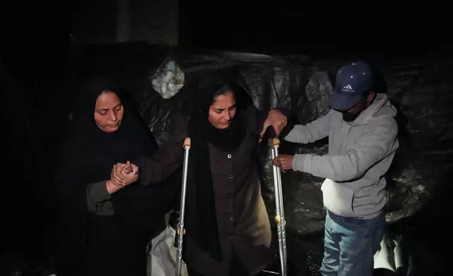 Rimas Abu Lehia, 15, who was injured in her left leg by Israeli fire, tries to sit on the ground with the help of her parents inside her family's tent in Khan Younis, Gaza Strip, Tuesday, Jan. 27, 2026, as she awaits permission to travel outside Gaza for medical treatment. (AP Photo/Abdel Kareem Hana)