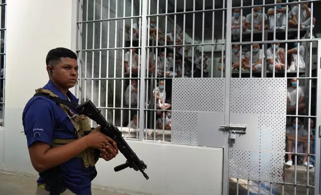A guard stands next to prisoners behind bars at the mega prison known as Detention Center Against Terrorism (CECOT) in Tecololuca, El Salvador, Friday, Jan. 30, 2026, during a tour for Chile's President-elect Jose Antonio Kast. (AP Photo/Salvador Melendez)