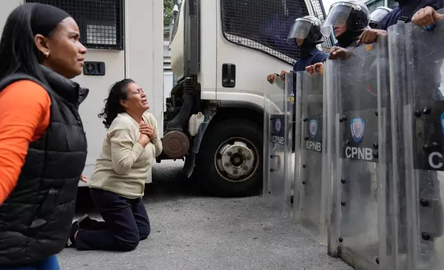 Relatives of people they consider to be detained for political reasons kneel in front of police guarding the Zona 7 Bolivarian National Police detention center in Caracas, Venezuela, Tuesday, Jan. 20, 2026. (AP Photo/Ariana Cubillos)