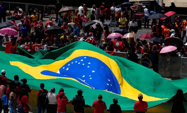 People hold open a large Brazilian flag during a ceremony marking the three year anniversary of a failed attempt to overthrow Brazil’s democratic system, at Planalto presidential palace in Brasilia, Brazil, Thursday, Jan. 8, 2026. (AP Photo/Eraldo Peres)