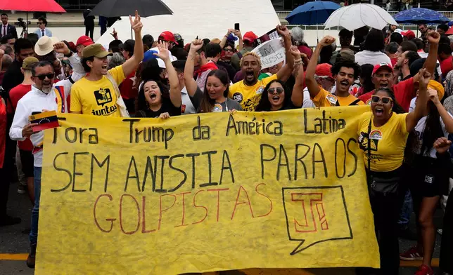 People carry a sign that reads in Portuguese: "Trump get out of Latin America" and "No amnesty for coup plotters" outside Planalto presidential palace on the three year anniversary of a failed attempt to overthrow Brazil’s democratic system, in Brasilia, Brazil, Thursday, Jan. 8, 2026. (AP Photo/Eraldo Peres)