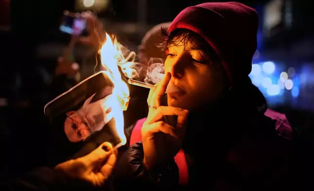 A protester smokes a cigarette after lighting it off a burning poster of Iran's Supreme Leader Ayatollah Ali Khamenei during a demonstration in Berlin, Germany, in support of the nationwide mass protests in Iran against the government, Wednesday, Jan. 14, 2026. (AP Photo/Ebrahim Noroozi)
