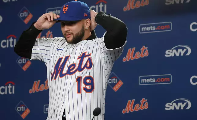 Bo Bichette puts on his hat and jersey during his introductory press conference with the New York Mets, Wednesday, Jan. 21, 2026, in New York. (AP Photo/Heather Khalifa)