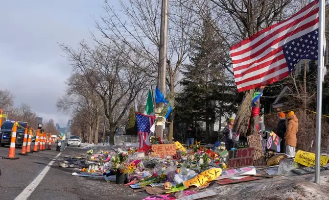 People stand near a memorial at the site where Renee Good was fatally shot by an ICE agent, Sunday, Jan. 11, 2026, in Minneapolis. (AP Photo/Jen Golbeck)