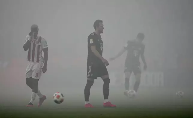 Bayern's Harry Kane, center, walks on the pitch covered in smoke from flares during the German Bundesliga soccer match between 1.FC Koeln and FC Bayern Munich in Cologne, Germany, Wednesday, Jan. 14, 2026. (AP Photo/Martin Meissner)