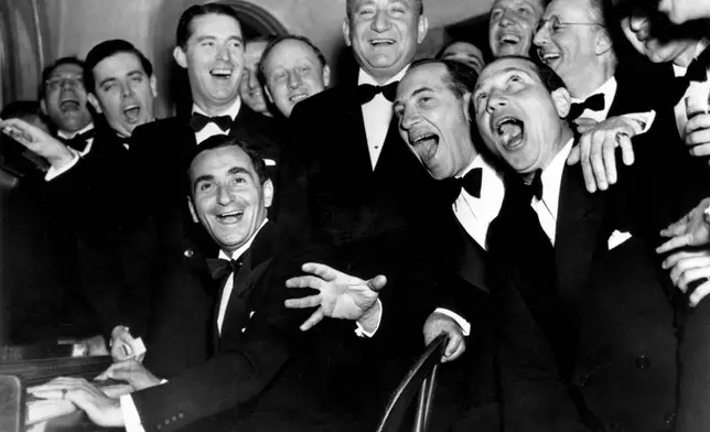 FILE - Irving Berlin, at the piano, and friends celebrate his 25th year since he wrote "Alexander's Rag Time Band" at a banquet in his honor in Hollywood, Ca., Jan. 20, 1936. Standing behind Berlin, at right, is Joseph Schenck, film producer. In front row singing together are two of the Marx Brothers, Chico and Harpo. (AP Photo, File)