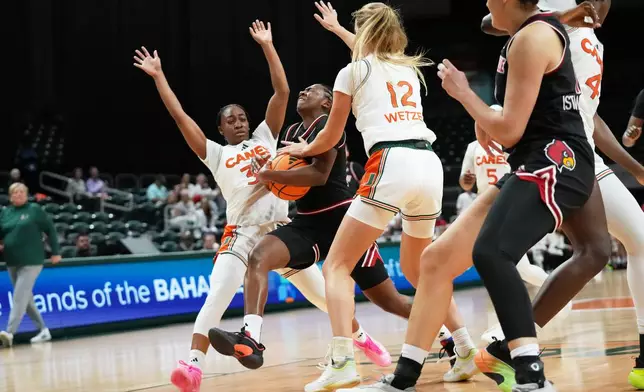 Louisville guard Reyna Scott, center, drives to the basket as Miami guard Amarachi Kimpson, left, and forward Natalie Wetzel (12) defend during the first half of an NCAA college basketball game, Thursday, Jan. 8, 2026, in Coral Gables, Fla. (AP Photo/Lynne Sladky)