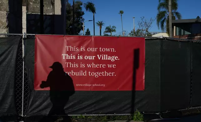 A person casts a shadow on a fence in front of a sign on the one-year anniversary of the Palisades Fire in the Pacific Palisades neighborhood of Los Angeles Wednesday, Jan. 7, 2026. (AP Photo/Jae C. Hong)