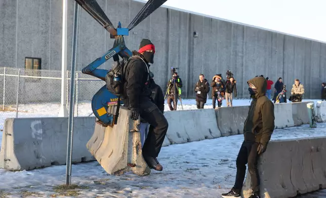 Protesters sit on a barrier that is being assembled outside the Bishop Henry Whipple Federal Building as demonstrators gather in Minneapolis, Friday, Jan. 9, 2026. (AP Photo/Adam Bettcher)
