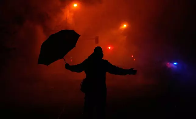 A protester holds an umbrella as they react to tear gas after a shooting on Wednesday, Jan. 14, 2026, in Minneapolis. (AP Photo/John Locher)
