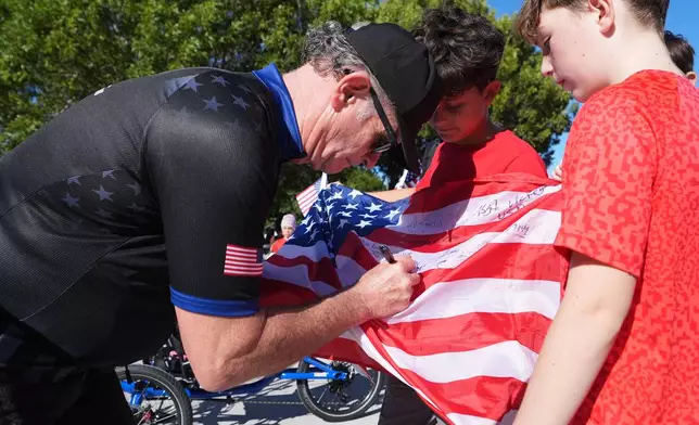 Wounded Warriors Project CEO Walt Piatt, left, signs an American flag for students outside of the Coral Shores High School as wounded veterans ride in the annual Florida Keys Soldier Ride organized by the Wounded Warrior Project, Friday, Jan. 9, 2026, in Islamorada, Fla. (AP Photo/Lynne Sladky)