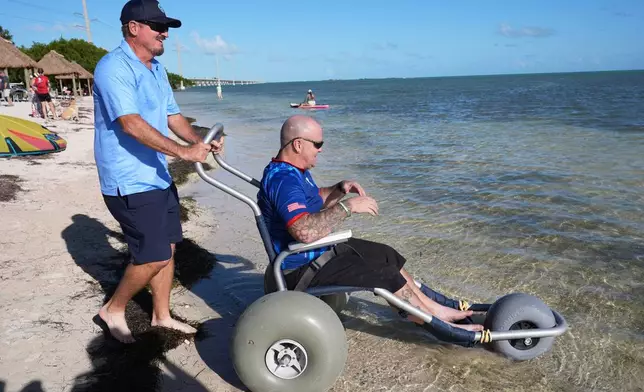 U.S. Navy veteran Jerry Padgett, right, is wheeled into the ocean at the Veterans Memorial Park after riding in the annual Florida Keys Soldier Ride organized by the Wounded Warrior Project, Friday, Jan. 9, 2026, in Little Duck Key, Fla. (AP Photo/Lynne Sladky)