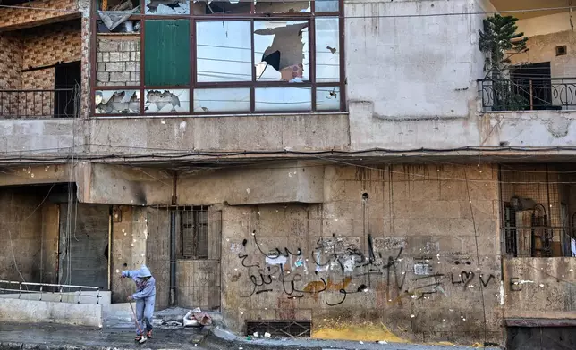 A Syrian girl sweeps debris along a street lined with damaged buildings in the Achrafieh neighborhood after a ceasefire was announced following three days of clashes between government forces and Kurdish fighters in a contested area of the northern city of Aleppo, Syria, Friday, Jan. 9, 2026. (AP Photo/Ghaith Alsayed)