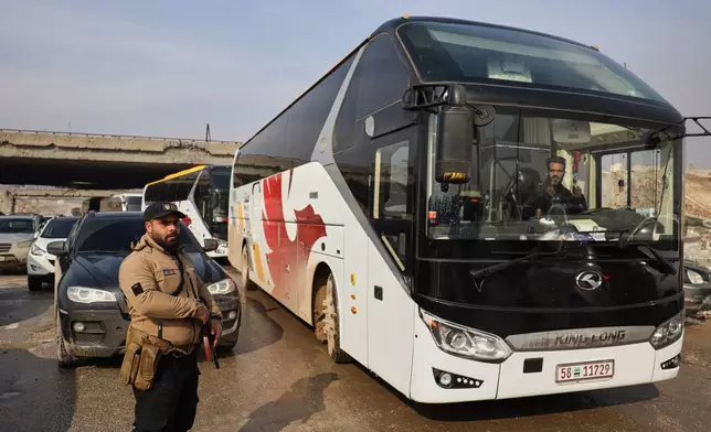 Members of Syrian government forces stand around buses prepared to evacuate Kurdish militants, under escort to the country's northeast, controlled by the SDF, after a ceasefire was announced following days of clashes in the northern city of Aleppo, Syria, Friday, Jan. 9, 2026. (AP Photo/Omar Albam)