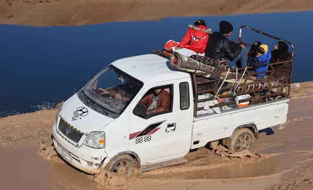 A displaced Syrian family rides in the back of a truck near a humanitarian crossing declared by the Syrian army next to a river in the village of Rasm Al-Abboud, in the eastern Aleppo countryside, near the front line with the Kurdish-led Syrian Democratic Forces in Deir Hafer, Syria, Thursday, Jan. 15, 2026. (AP Photo/Omar Albam)