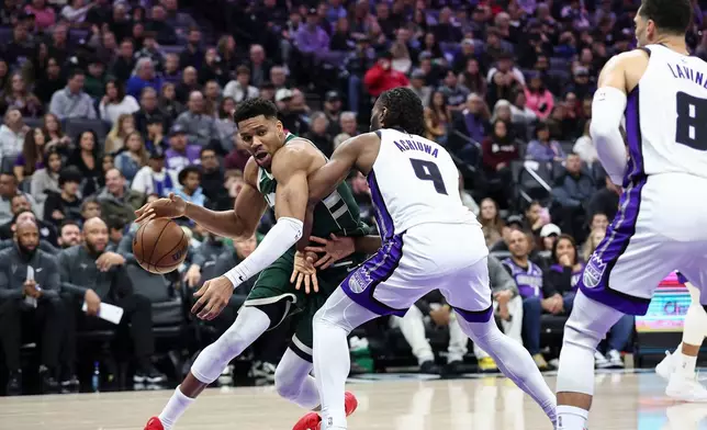 Milwaukee Bucks forward Giannis Antetokounmpo, left, drives to the basket with Sacramento Kings forward Precious Achiuwa (9) defending during the first half of an NBA basketball game, Sunday, Jan. 4, 2026, in Sacramento, Calif. (AP Photo/Sara Nevis)
