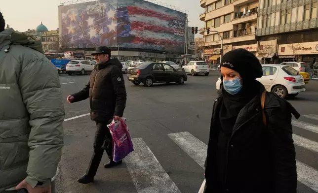 People walk past a billboard depicting a damaged U.S. aircraft carrier with disabled fighter jets on its deck and a sign reading in Farsi and English, "If you sow the wind, you'll reap the whirlwind," at Enqelab-e-Eslami (Islamic Revolution) Square in Tehran, Iran, Sunday, Jan. 25, 2026. (AP Photo/Vahid Salemi)