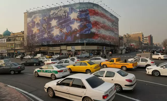 Vehicles drive past a billboard depicting a damaged U.S. aircraft carrier with disabled fighter jets on its deck and a sign reading in Farsi and English, "If you sow the wind, you'll reap the whirlwind," at Enqelab-e-Eslami (Islamic Revolution) Square in Tehran, Iran, Sunday, Jan. 25, 2026. (AP Photo/Vahid Salemi)