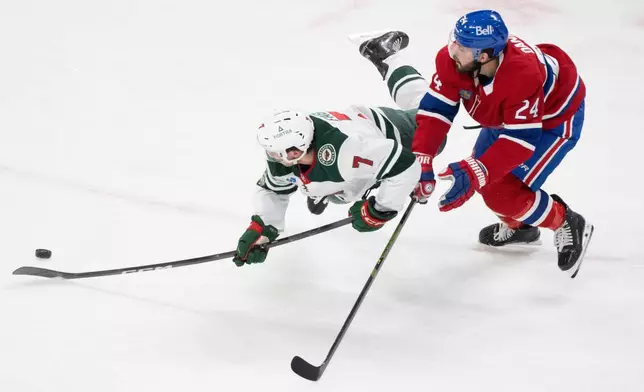 Minnesota Wild's Brock Faber (7) is tripped up by Montreal Canadiens' Phillip Danault (24) during the first period of an NHL hockey game in Montreal, Tuesday, Jan. 20, 2026. (Christinne Muschi/The Canadian Press via AP)