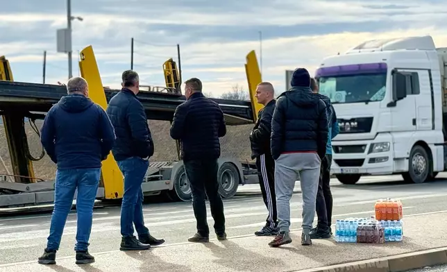 Men stand next to a line of trucks and buses on the Bosnian side of the border with Croatia, in Svilaj, Bosnia, Monday, Jan. 26, 2026, as drivers across the Balkans blocked dozens of border crossings in the region in protest over newly introduced European Union entry regulations.(AP Photo/Eldar Emric)