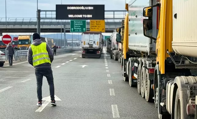A man stands next to a line of trucks and buses on the Bosnian side of the border with Croatia, in Svilaj, Bosnia, Monday, Jan. 26, 2026, as drivers across the Balkans blocked dozens of border crossings in the region in protest over newly introduced European Union entry regulations.(AP Photo/Eldar Emric)