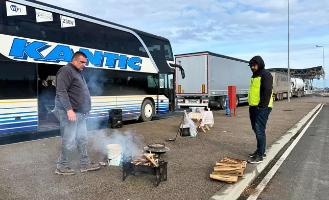 A man prepares to cook on a portable grill next to a line of trucks and buses on the Bosnian side of the border with Croatia, in Svilaj, Bosnia, Monday, Jan. 26, 2026, as drivers across the Balkans blocked dozens of border crossings in the region in protest over newly introduced European Union entry regulations.(AP Photo/Eldar Emric)