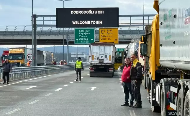 Men stand next to a line of trucks and buses on the Bosnian side of the border with Croatia, in Svilaj, Bosnia, Monday, Jan. 26, 2026, as drivers across the Balkans blocked dozens of border crossings in the region in protest over newly introduced European Union entry regulations.(AP Photo/Eldar Emric)