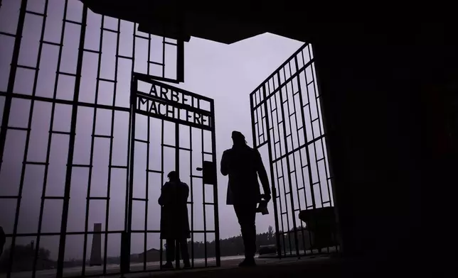 Two men enter the Nazi Concentration Camp Sachsenhausen through a gate with writing "Arbeit macht frei" in German reading "Work makes free", on the eve on the International Holocaust Memorial Day in Oranienburg, Germany, Monday, Jan. 26, 2026. (AP Photo/Markus Schreiber)
