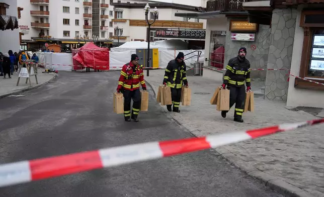 Firefighters carry equipment near the sealed off Le Constellation bar in Crans-Montana, Swiss Alps, Switzerland, Friday, Jan. 2, 2026, where a devastating fire left dead and injured during the New Year's celebrations. (AP Photo/Baz Ratner)