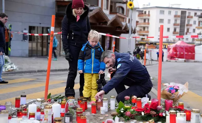 A police officer helps a boy to light a candle near the sealed off Le Constellation bar in Crans-Montana, Swiss Alps, Switzerland, Friday, Jan. 2, 2026, where a devastating fire left dead and injured during the New Year's celebrations. (AP Photo/Baz Ratner)