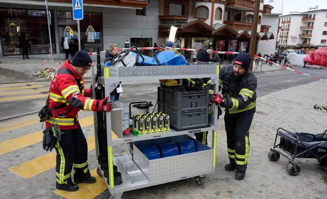 Firefighters pull a trolley with equipment near the sealed off Le Constellation bar in Crans-Montana, Swiss Alps, Switzerland, Friday, Jan. 2, 2026, where a devastating fire left dead and injured during the New Year's celebrations. (AP Photo/Baz Ratner)
