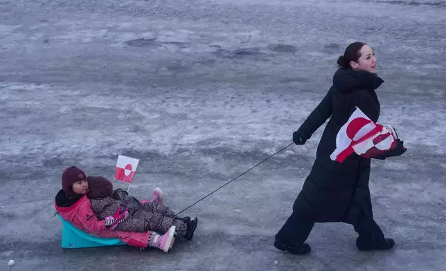 A woman pulls her children on a sled during a protest against Trump's policy towards Greenland in front of the US consulate in Nuuk, Greenland, Saturday, Jan. 17, 2026. (AP Photo/Evgeniy Maloletka)