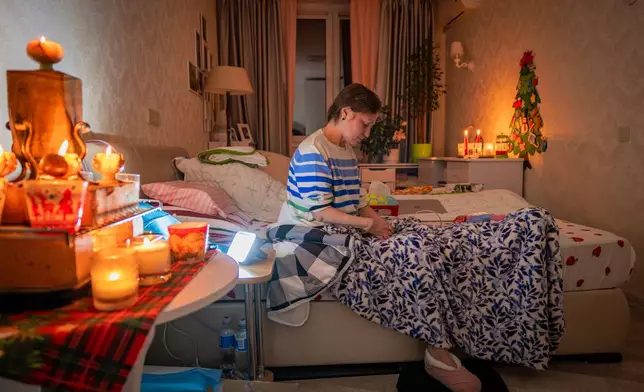 Kyiv resident Olena Janchuk, 53, who can no longer walk due to illness, endures a blackout in her apartment with her mother, keeping warm with candles and heated bricks after Russian attacks on Ukraine's energy infrastructure in Kyiv, Ukraine, Tuesday, Jan. 20, 2026. (AP Photo/Dan Bashakov)