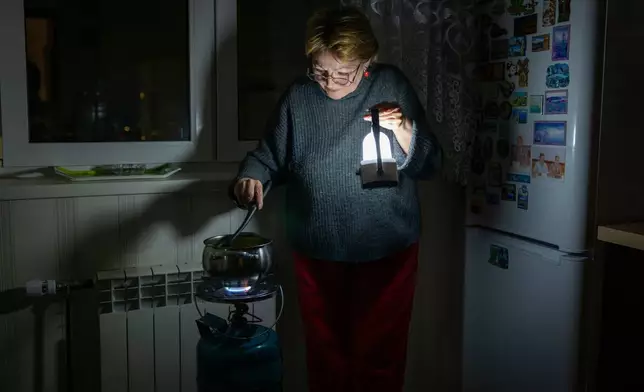 Olena Janchuk's mother cooks food on a gas burner by lantern light during a blackout in Kyiv following Russian attacks on energy infrastructure in Kyiv, Ukraine, Tuesday, Jan. 20, 2026. (AP Photo/Dan Bashakov)