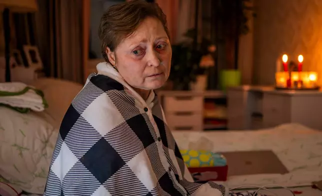 Kyiv resident Olena Janchuk, 53, who can no longer walk due to illness, endures a blackout in her apartment with her mother, keeping warm with candles and heated bricks after Russian attacks on Ukraine's energy infrastructure in Kyiv, Ukraine, Tuesday, Jan. 20, 2026. (AP Photo/Dan Bashakov)