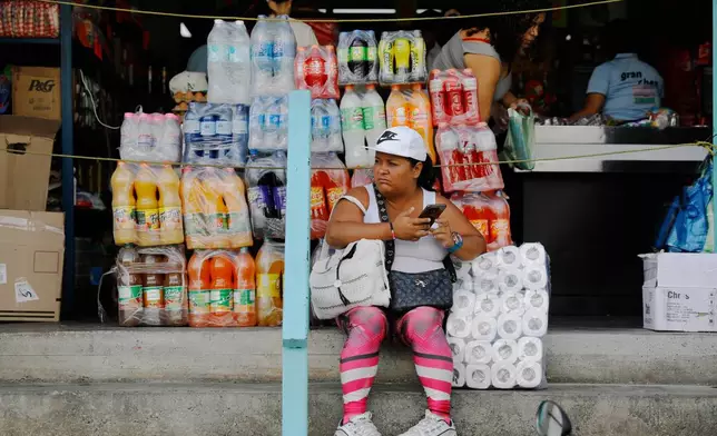 A woman sits in front of a store in the Petare neighborhood of Caracas, Venezuela, Wednesday, Jan. 7, 2026. (AP Photo/Cristian Hernandez)