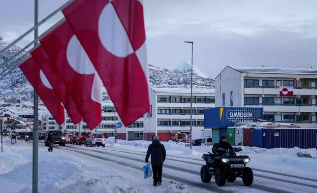 A man rides by on a quad bike past a row of Greenlandic national flags in Nuuk, Greenland, Wednesday, Jan. 14, 2026. (AP Photo/Evgeniy Maloletka)