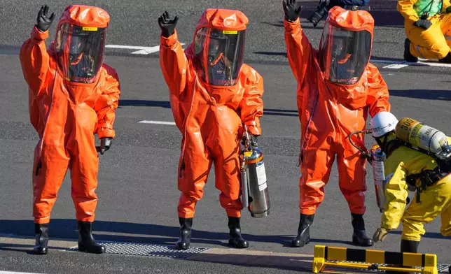 Members of firefighters with full-body hazardous materials protective suits, raise arms during the annual New Year's Fire Brigade Review Tuesday, Jan. 6, 2026, in Tokyo. (AP Photo/Eugene Hoshiko)