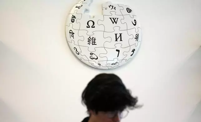 Emeline Brule, volunteer Wikipedia editor, sits below a Wikipedia logo displayed at the Wikimedia Foundation office in San Francisco, Monday, Jan. 12, 2026. (AP Photo/Jeff Chiu)