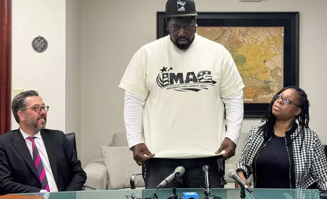 Garrison Gibson, a Liberian man who has lived in the U.S. for around three decades, shows reporters his shirt reading “Immigrants make America great” during a news conference Saturday, Jan. 17, 2026. (AP Photo/Jack Brook)