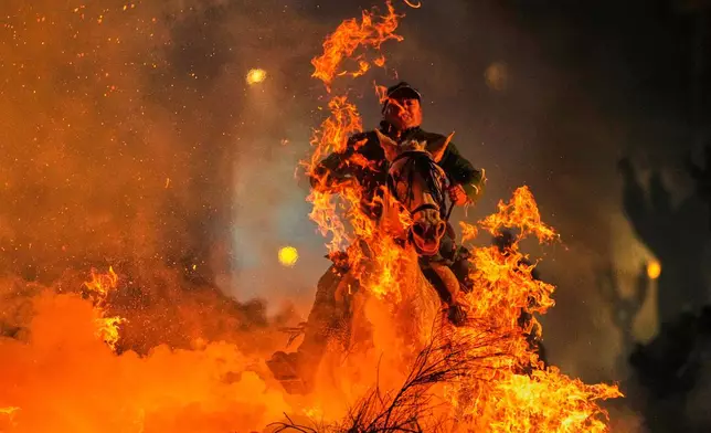 A man rides a horse through a bonfire as part of a ritual in honor of Saint Anthony the Abbot, the patron saint of domestic animals, in San Bartolome de Pinares, Spain, Friday, Jan. 16, 2026. (AP Photo/Manu Fernandez)