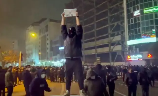 In this frame grab from video obtained by the AP outside Iran, a masked demonstrator holds a picture of Iran's Crown Prince Reza Pahlavi during a protest in Tehran, Iran, Friday, January. 9, 2026. (UGC via AP)
