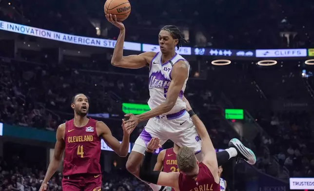 Utah Jazz forward Cody Williams, center, is called for an offensive foul on Cleveland Cavaliers guard Sam Merrill, bottom, as center Evan Mobley (4) looks on in the first half of an NBA basketball game in Cleveland, Monday, Jan. 12, 2026. (AP Photo/Sue Ogrocki)
