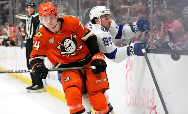 Anaheim Ducks defenseman Ian Moore, left, puts Tampa Bay Lightning defenseman Declan Carlile into the boards during the second period of an NHL hockey game Wednesday, Dec. 31, 2025, in Anaheim, Calif. (AP Photo/Mark J. Terrill)