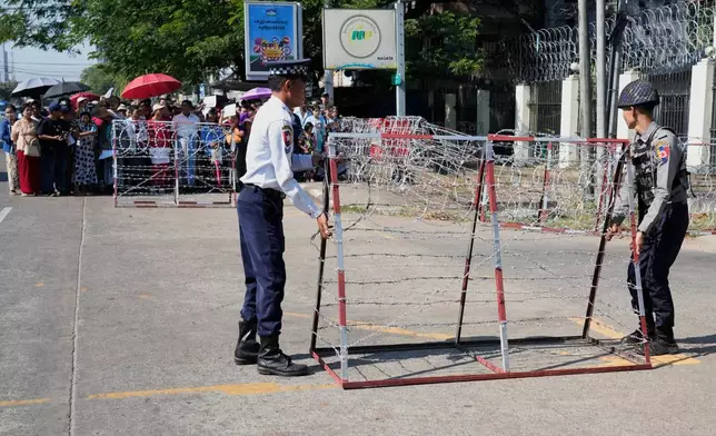 Polices set up a barricade while family members and colleagues wait to welcome the released prisoners from Insein Prison Sunday, Jan. 4, 2026, in Yangon, Myanmar. (AP Photo/Thein Zaw)