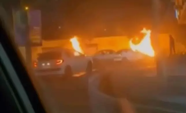 This frame grab from a video released Friday, Jan. 9, 2026, by Iranian state television shows cars driving past burning vehicles during a night of mass protests in Tehran, Iran. (Iranian state TV via AP)