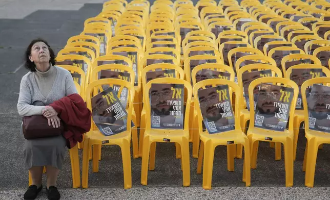 A woman sits for a moment by chairs with photos of Ran Gvili, the final hostage in Gaza who was killed while fighting Hamas militants during the Oct. 7, 2023 attack, on the same day his remains were recovered, in a plaza known as Hostages Square, in Tel Aviv, Israel, Monday, Jan. 26, 2026. (AP Photo/Oded Balilty)